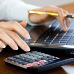 Picture of woman typing on a computer and calculator